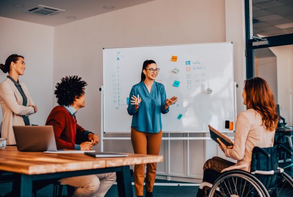 Happy entrepreneur talking to her coworkers about inclusive business strategy while holding presentation in the office.