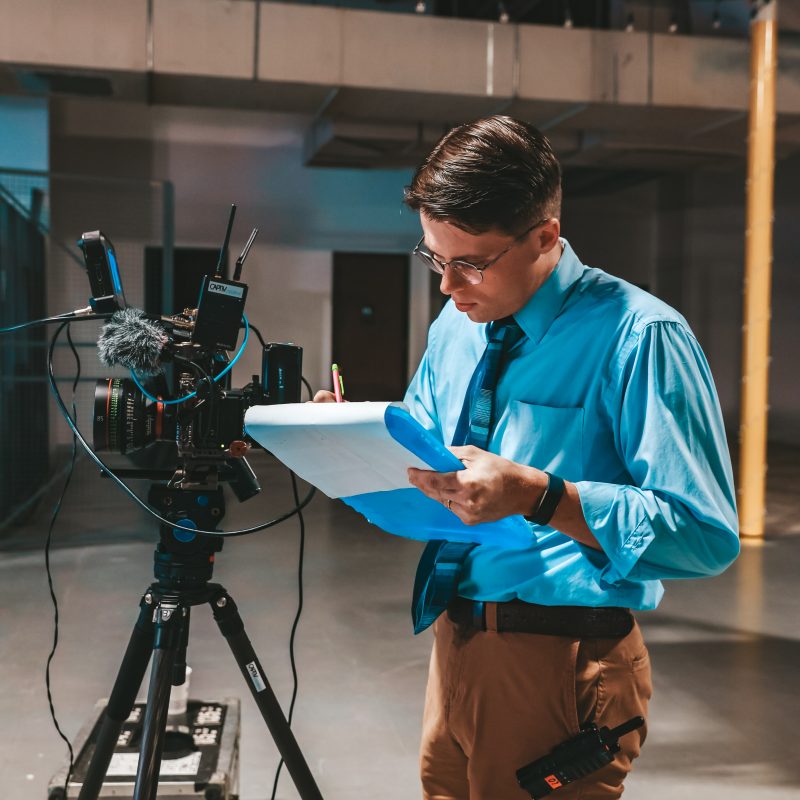 Video production director reviewing notes while standing next to a camera on a film set.